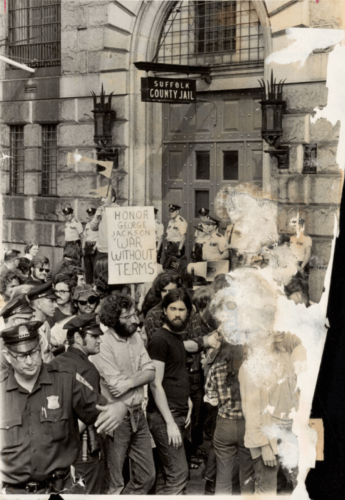 A black and white photographs of protestors standing outside the Suffolk County Jail.