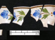 Fragments of pearlware ceramics against a black backdrop. They are cream-colored with blue flowers.