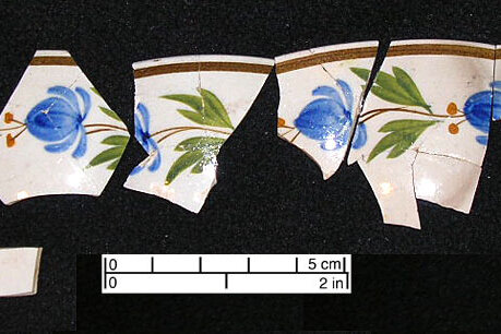 Ceramics, African Meeting House Fragments of pearlware ceramics against a black backdrop. They are cream-colored with blue flowers.