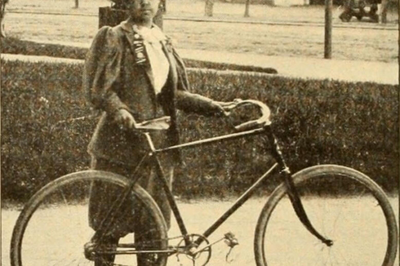 A black and white photograph of a Black woman holding a bicycle.