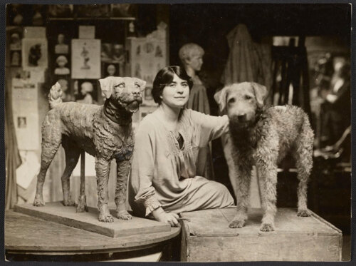 A black and white photograph of a seated woman next to a dog and a sculpture depicting the same dog.