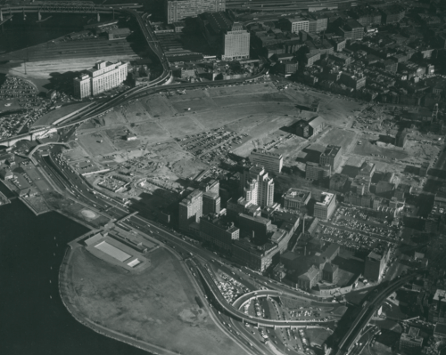 A black and white aerial photograph of a demolished neighborhood, with only a few buildings left standing.