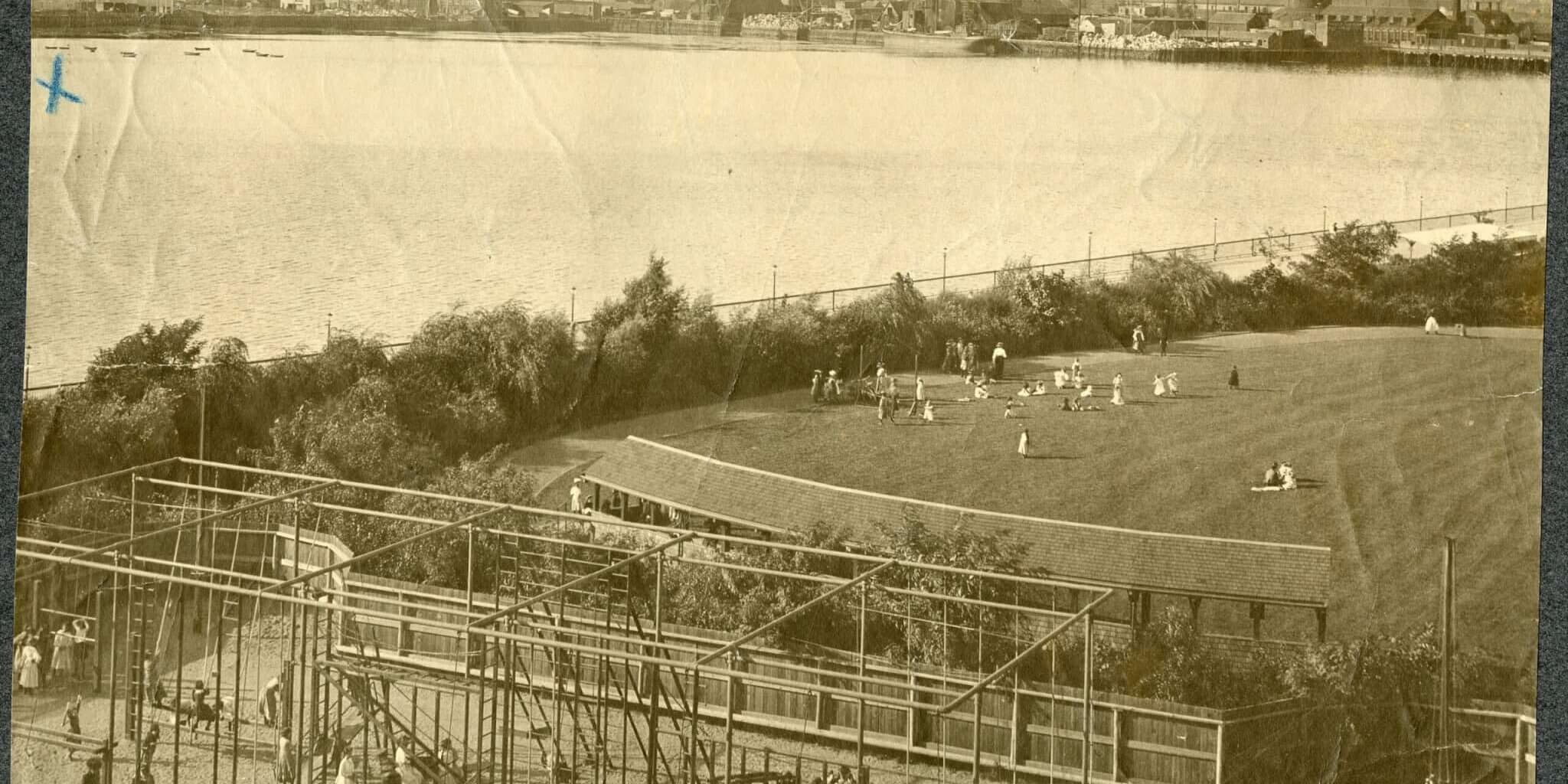 womens_gym(1897)(Olmsted_shurtleff) Sepia image of a gymnasium structure and lawn on the edge of a river.