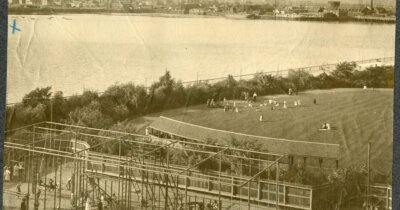 Sepia image of a gymnasium structure and lawn on the edge of a river.