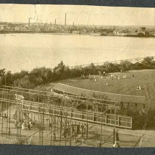 Sepia image of a gymnasium structure and lawn on the edge of a river.