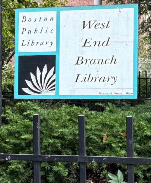 Image of a sign for the West End Branch of the Boston Public library above shrubbery and a metal fence.