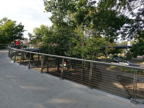 An image of a paved bridge with wire railings overlooking trees.