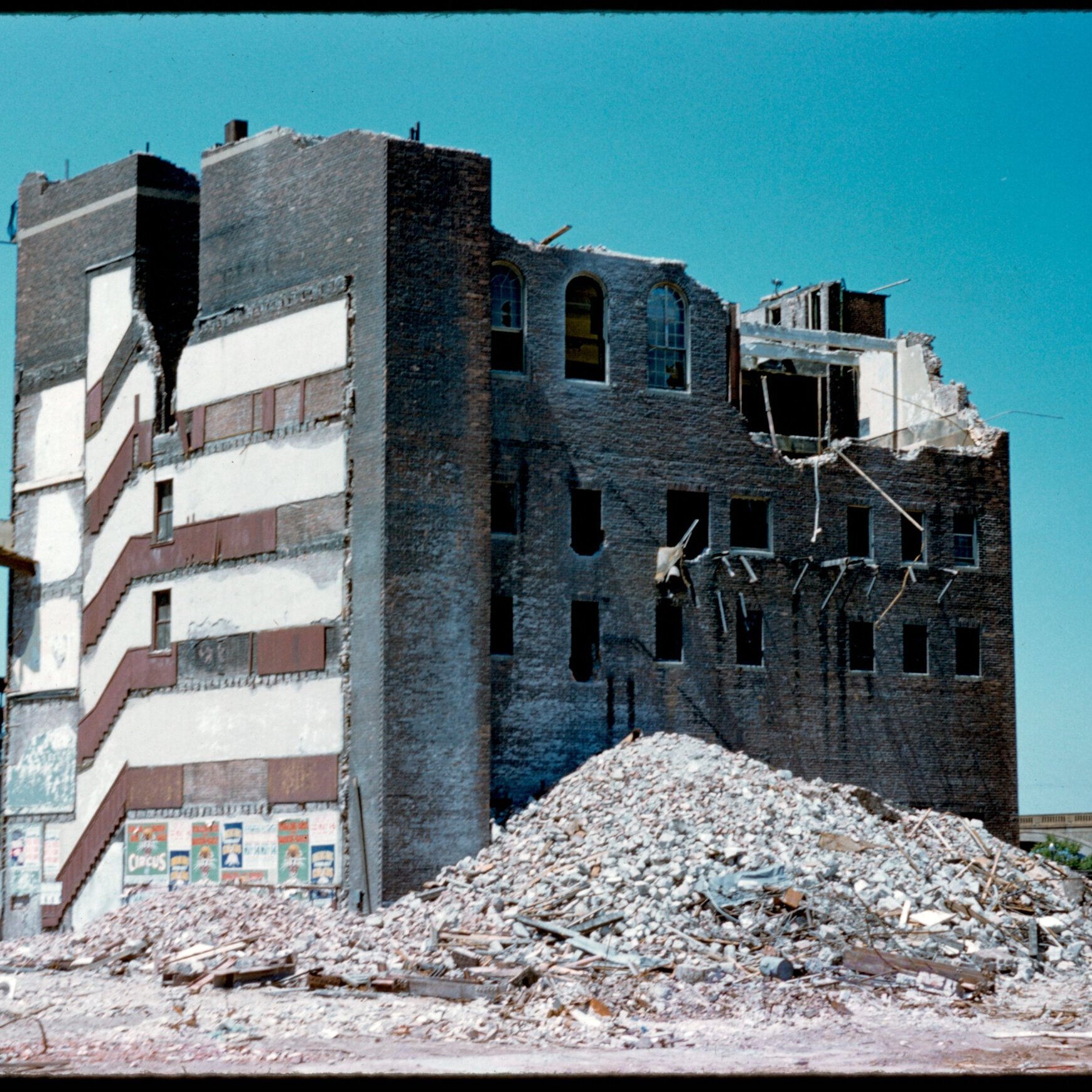 A half demolished building with circus advertisements along an exposed stairwell.