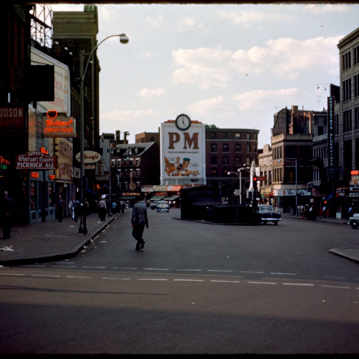 An image of a city square with a subway entrance and buildings with neon signs.