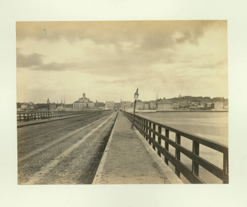 A photograph of a flat bridge with a lamppost and a city skyline in the distance.