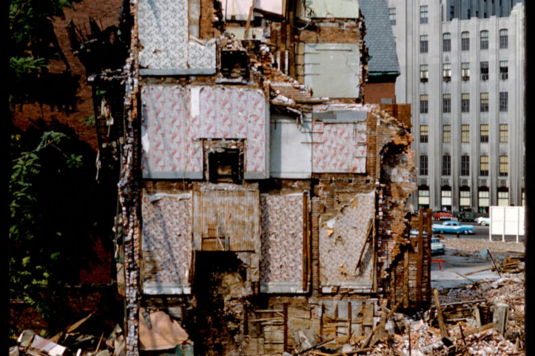 A half demolished building with different rooms with colorful wallpaper visible.