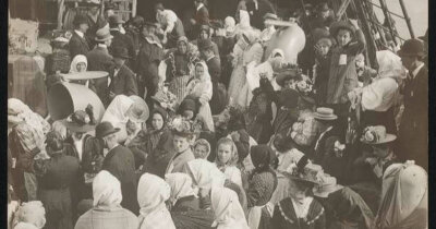 A crowd of people on the deck of a ship dressed in early 20th century clothing.