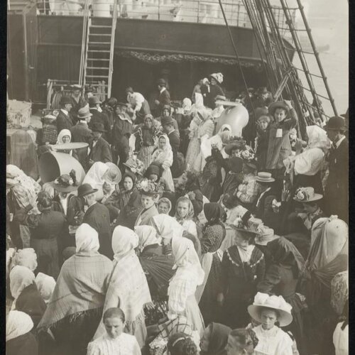 A crowd of people on the deck of a ship dressed in early 20th century clothing.