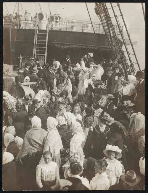 A crowd of people on the deck of a ship dressed in early 20th century clothing.