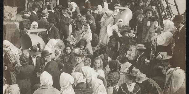 Immigrants on a boat. A crowd of people on the deck of a ship dressed in early 20th century clothing.