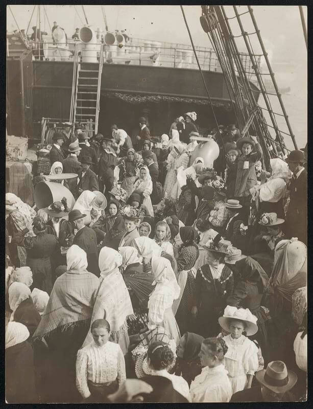 Immigrants on a boat. A crowd of people on the deck of a ship dressed in early 20th century clothing.