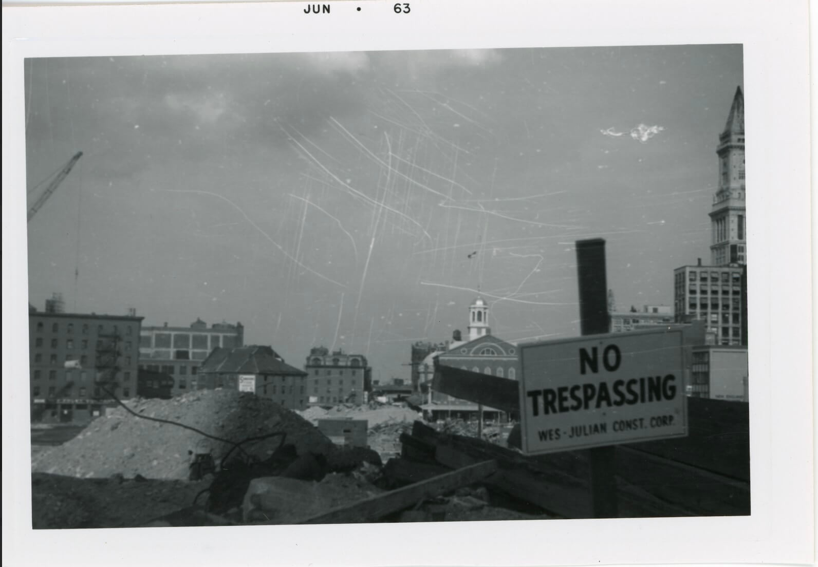 A pile of rubble with a "No Trespassing" sign with buildings in the background.