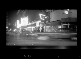 A grainy image of a street corner lit by neon.