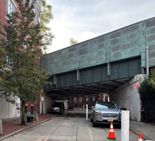 A green metal bridge crossing over a street with a car underneath.