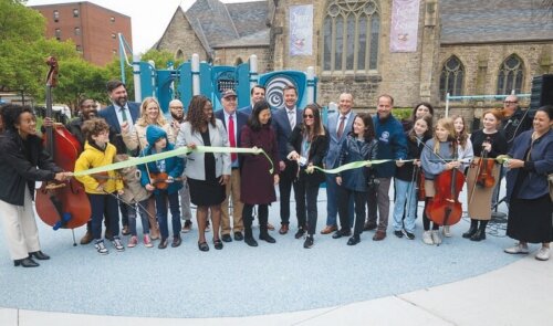 A group of adults and children cutting a ribbon in front of a playground.