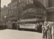 A crowd of people standing next to a group of women on a bus underneath a theatre marquee.