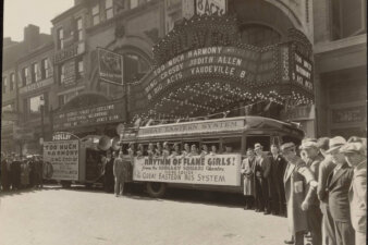 A crowd of people standing next to a group of women on a bus underneath a theatre marquee.