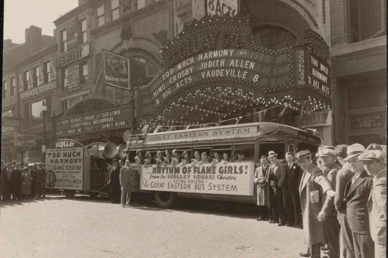 A crowd of people standing next to a group of women on a bus underneath a theatre marquee.