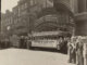 A crowd of people standing next to a group of women on a bus underneath a theatre marquee.