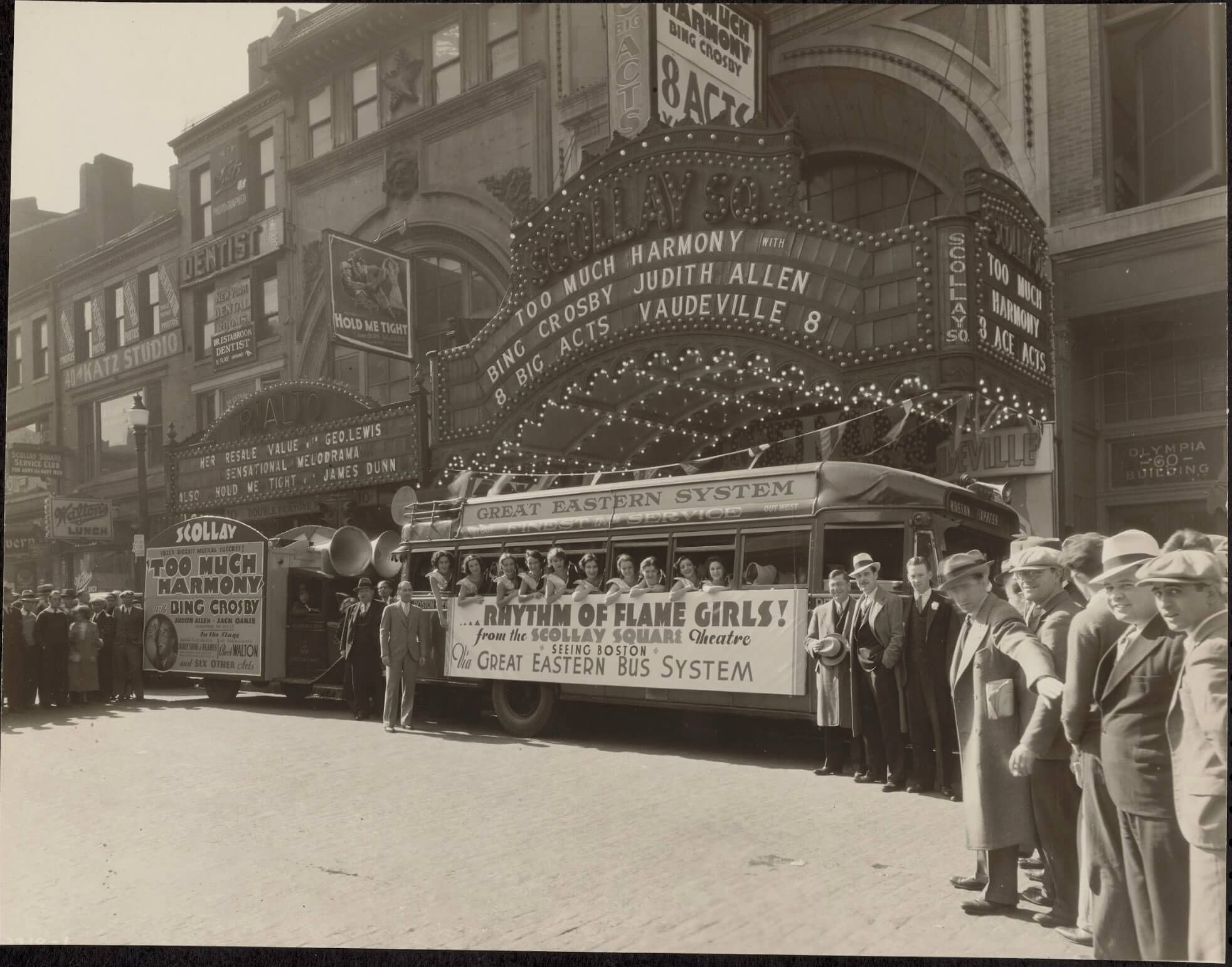 A crowd of people standing next to a group of women on a bus underneath a theatre marquee.