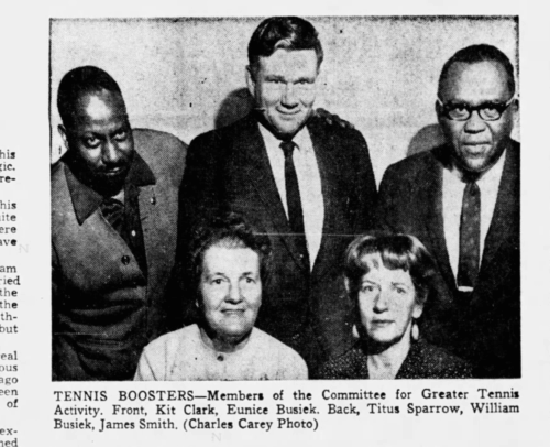 Three men standing and two women standing in an image in a newspaper.