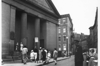 A group of parishioners climbing the steps of a church while a policeman looks on.