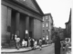 A group of parishioners climbing the steps of a church while a policeman looks on.