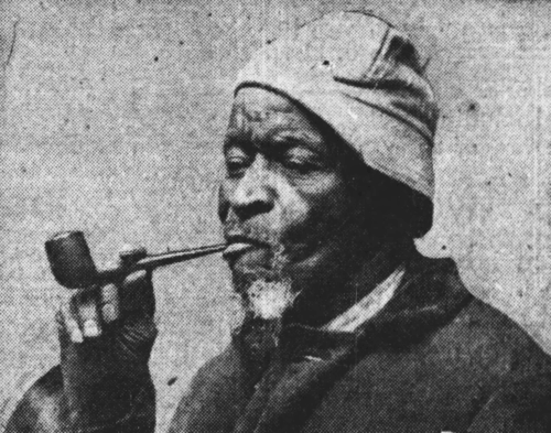 An elderly man wearing a hat smoking a pipe.