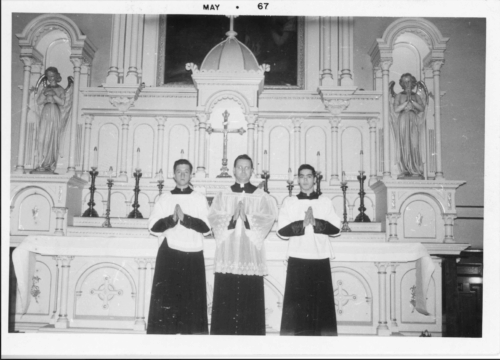 A priest standing between two altar boys in front of a catholic altar.