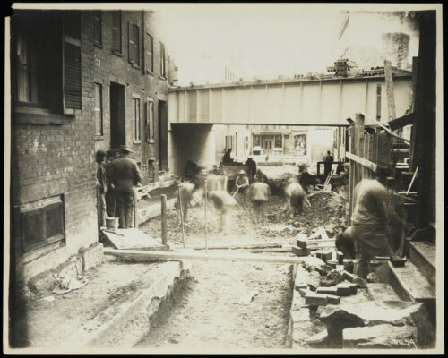 Construction workers creating an overpass on a narrow street.