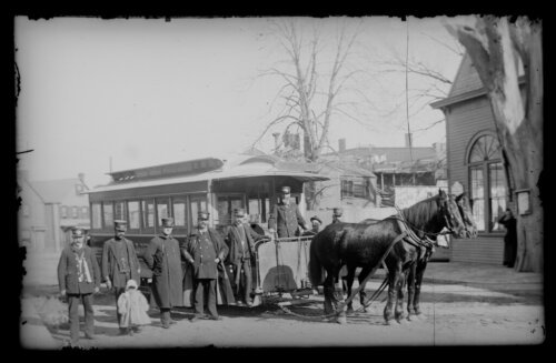 A group of men and a small child stand near a horse-pulled omnibus.