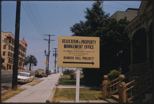 A sign pointing to the right between a sidewalk and a row of houses.