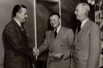 Three men standing with two shaking hands.