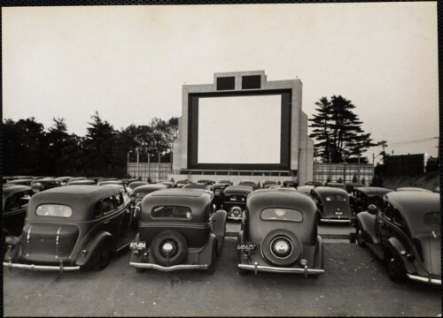 1950s cars parked in front of an outdoor movie screen.