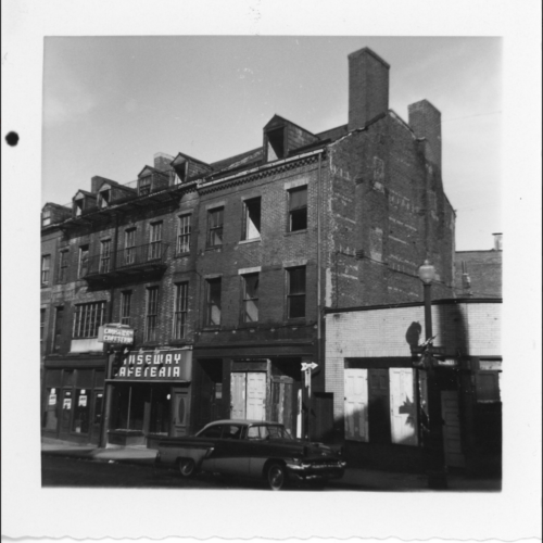A city street with several three story buildings one of which has a sign that says Causeway Cafeteria.