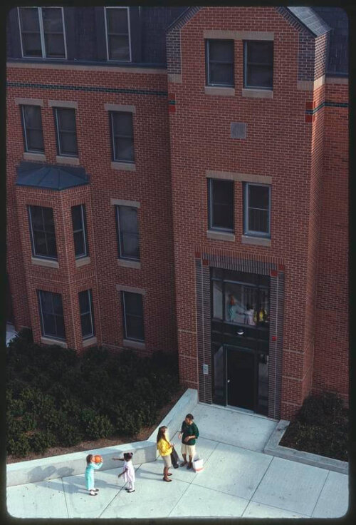 A group of people walking into a mid-rise brick apartment building.