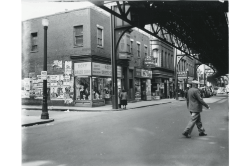 A man walking under an elevated railroad next to a street corner.