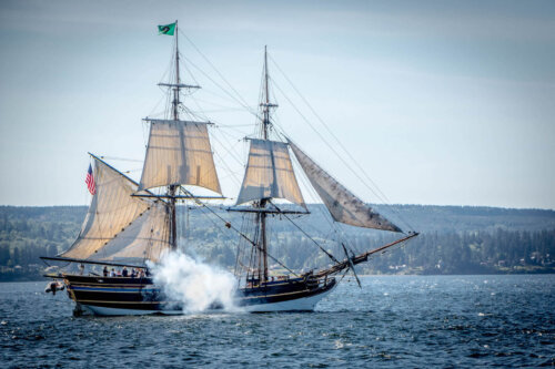 A two-masted ship firing a cannon on the water.