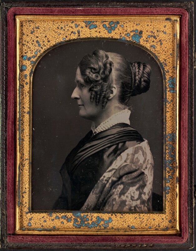 A portrait of a woman facing to the left with a bun and elaborate curls at the side of her face.
