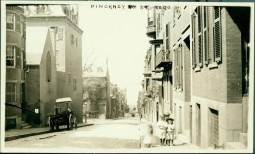 Two small children pose in front of the camera on a street full of brick buildings.