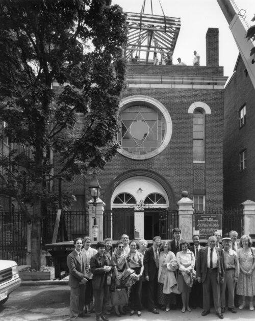 A group of people standing in front of a building while a crane lowers a skylight into place.