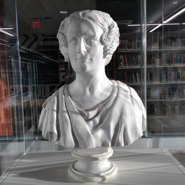A bust of a woman with curls on the side of her face in a library.