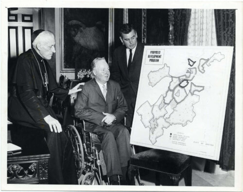 A priest, a man in a wheelchair, and a third man look at a map of Boston.