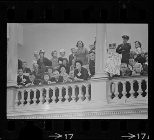 A large crowd of men and women watching from a balcony holding protest signs.