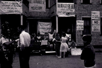 People standing in front of a triple decker home decorated with protest signs.